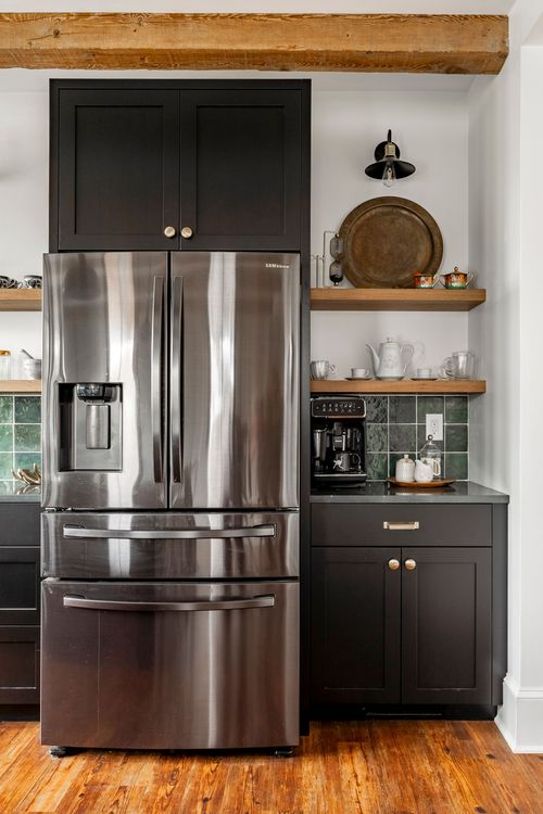 Close view of a stainless French-door refrigerator between dark cabinetry and wood shelving