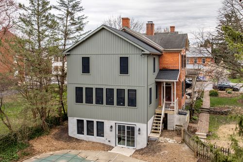 Aerial view of a three-story gray home addition with black-framed windows beside a brick colonial