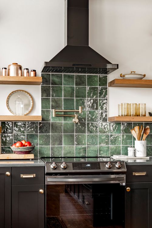 Close view of a green tile backsplash with pot-filler faucet, copper canisters and black range