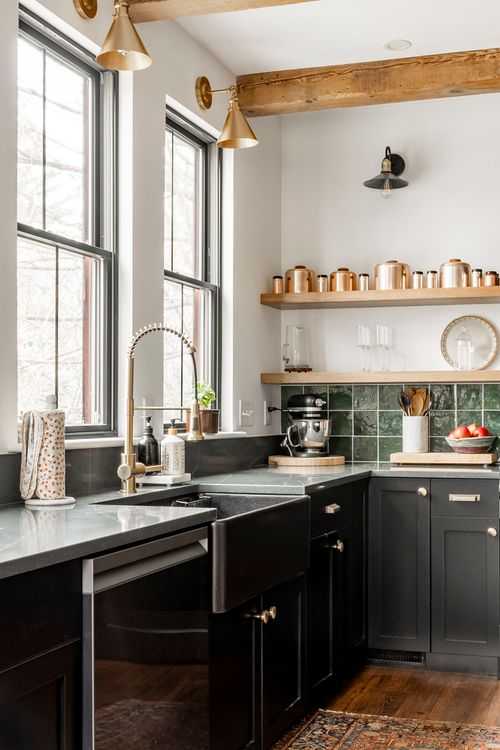 Kitchen corner with a black farmhouse sink, brass faucet, gold sconces and copper canisters