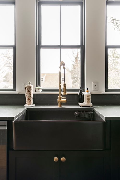 Black farmhouse sink with a brass faucet under three tall windows