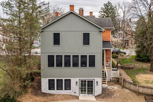 Aerial view of a gray gabled addition with a screened porch, deck stairs and mature trees