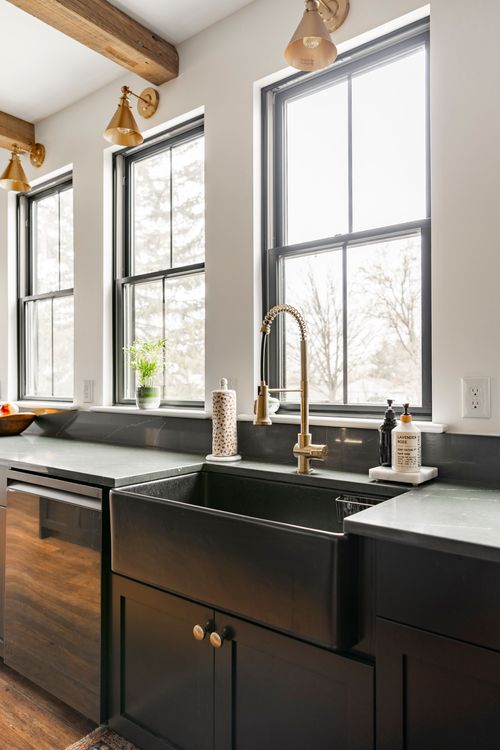 Black farmhouse sink with a brass gooseneck faucet and green soapstone counters