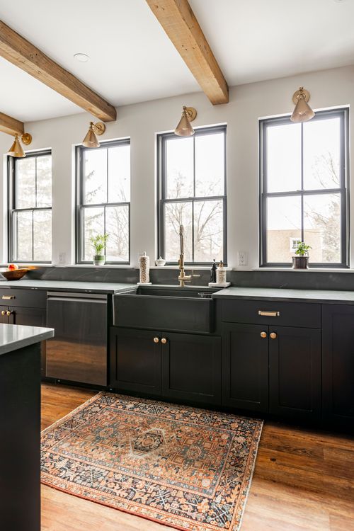 Black farmhouse sink under four windows with brass sconces and a vintage runner rug