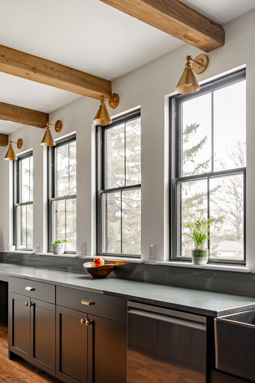 Kitchen counter along windows with brass sconces, soapstone counter and wood ceiling beams