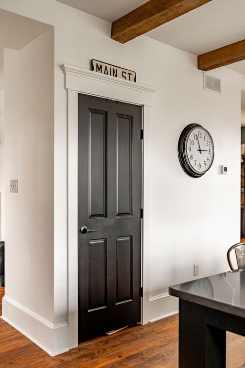 Hallway with a black paneled door, MAIN ST sign and a round wall clock