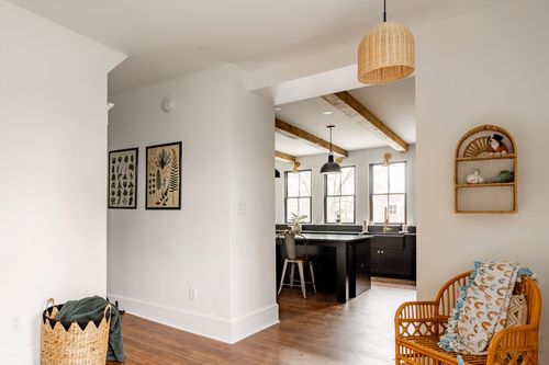 Hallway with botanical art, a rattan bench and a wood beam kitchen visible beyond