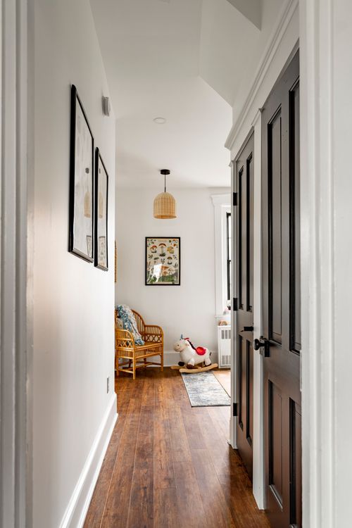 Hallway with black paneled doors, framed prints, a woven pendant and a rocking horse