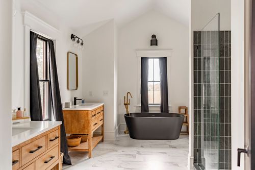Vaulted primary bath with wood vanities, a black soaking tub and dark tiled walk-in shower