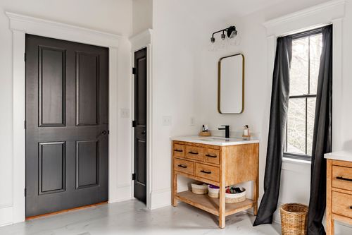 Bathroom with a black paneled door, wood vanity, brass mirror and black curtain