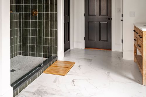 Dark green tiled walk-in shower beside a marble floor and wood bath mat