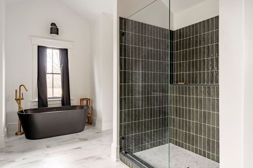 Black freestanding tub with a brass faucet beside a dark tiled walk-in shower