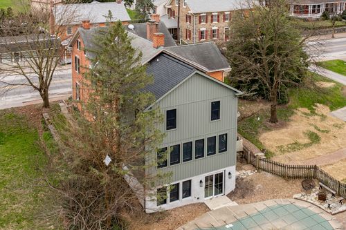 Aerial view of a gray-sided addition framed by evergreens beside a red-brick historic house