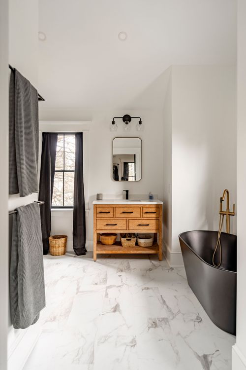 Bathroom with a wood vanity, round mirror and a black freestanding tub in the corner