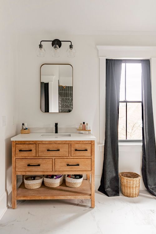 Wood bathroom vanity with a round mirror, black sconce and woven storage baskets