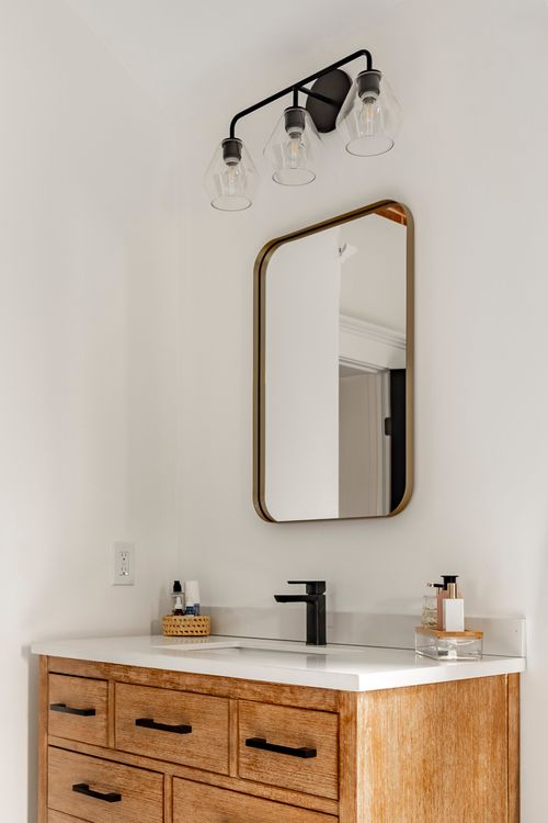 Wood vanity detail with a matte-black faucet and an arched brass mirror