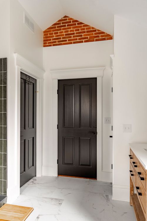 Bathroom hallway with black paneled doors under an exposed brick gable peak