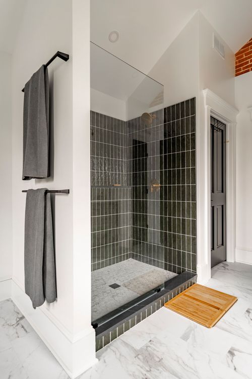 Dark tiled walk-in shower with black towel bars and a teak bath mat