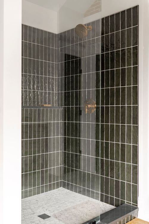 Dark green tiled shower corner with a brass shower head and marble floor tile