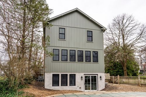 Exterior of a gray board-and-batten home addition with black windows and a white masonry base