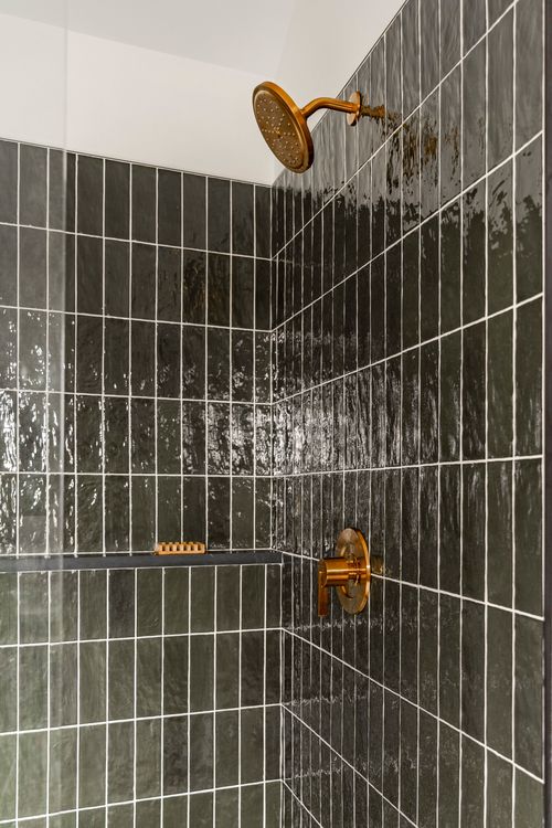 Close view of a brass shower head and handle set against dark green tile