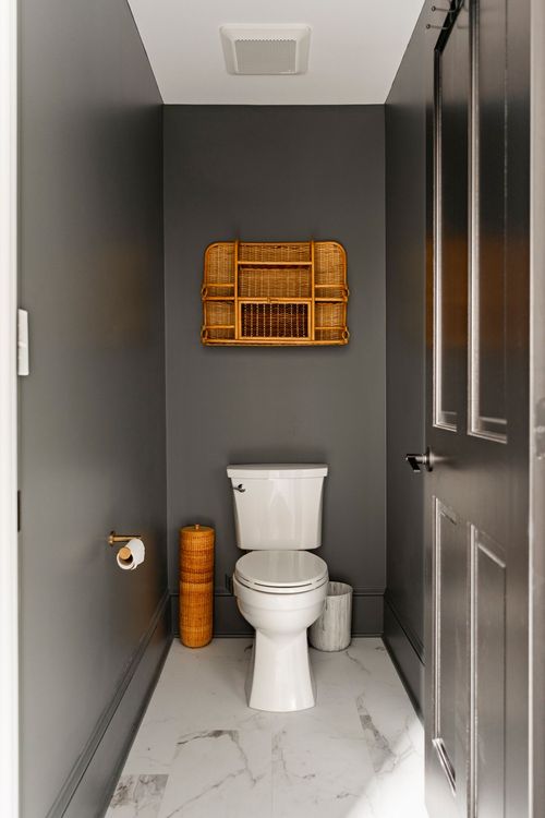Charcoal powder room with a wall-mounted toilet, rattan shelf and marble floor