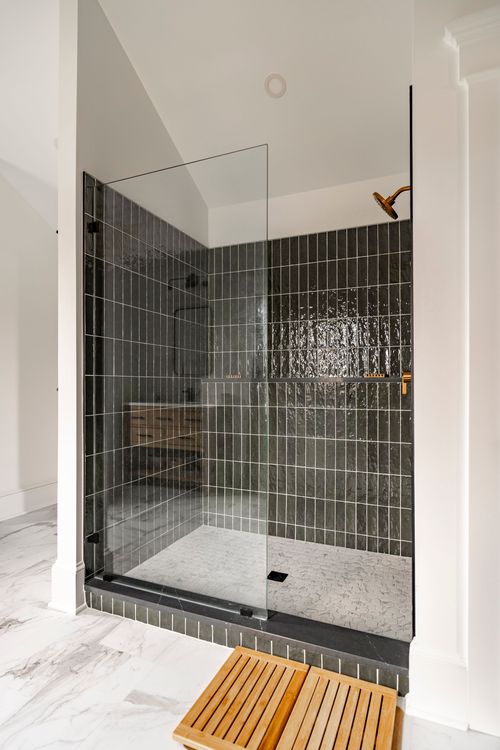Dark tiled walk-in shower with a glass panel door and built-in wood bench