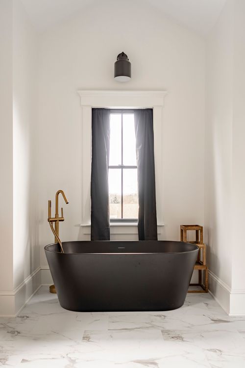 Vaulted bathroom nook with a black soaking tub, brass faucet and curtained window