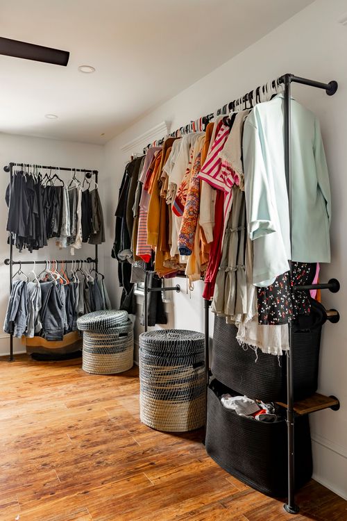 Walk-in closet with open pipe clothing racks and woven storage baskets
