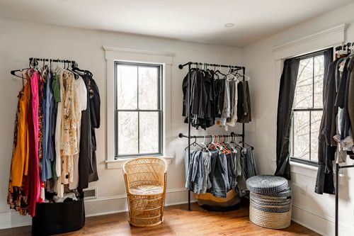 Walk-in closet with a rattan chair, open racks and windows on two walls