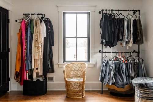 Walk-in closet with hanging clothes, a rattan chair and natural light from a window