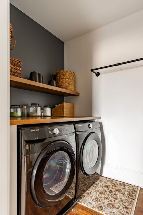 Laundry room with a black washer and dryer under open shelving and a dark accent wall