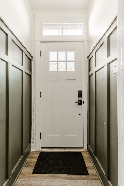 Entry hallway with a white paneled front door, dark wainscoting and a doormat