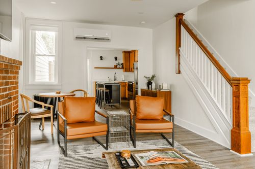 Living area with leather chairs, wood staircase and a kitchen visible beyond