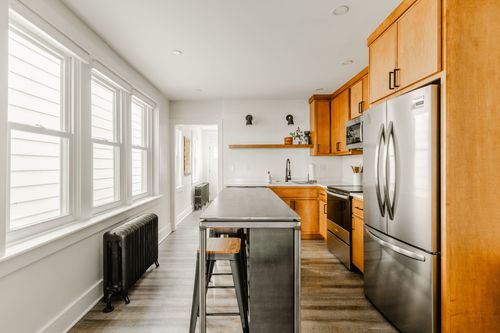 Kitchen with wood cabinetry, stainless refrigerator and a metal-topped island with stools