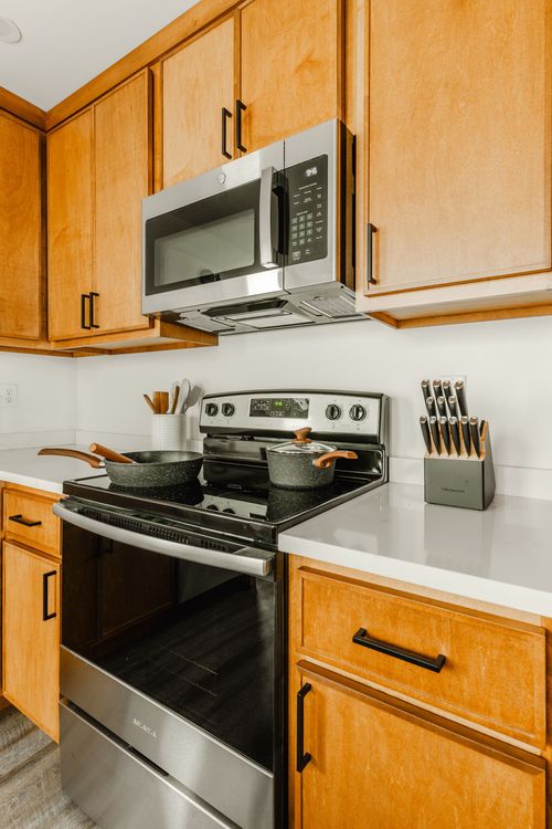 Close view of wood kitchen cabinets, stainless range and microwave with cookware