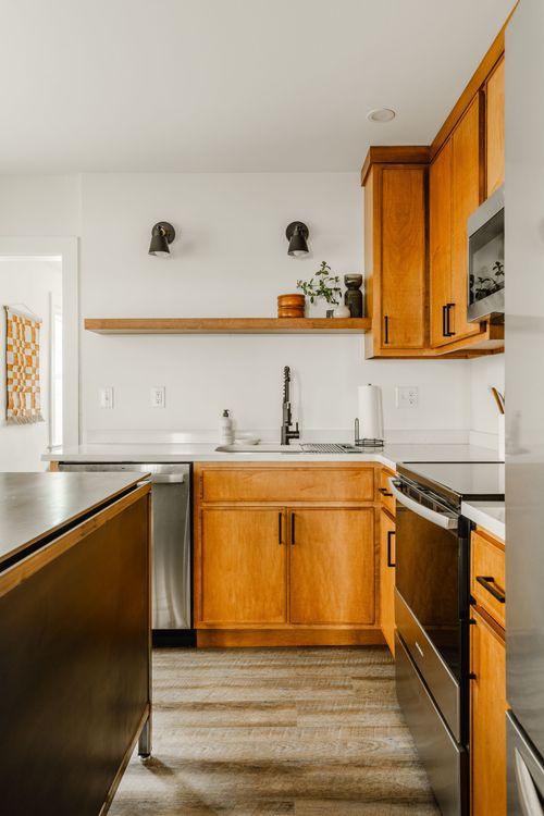 Kitchen sink area with wood cabinetry, white quartz counters and open wood shelving