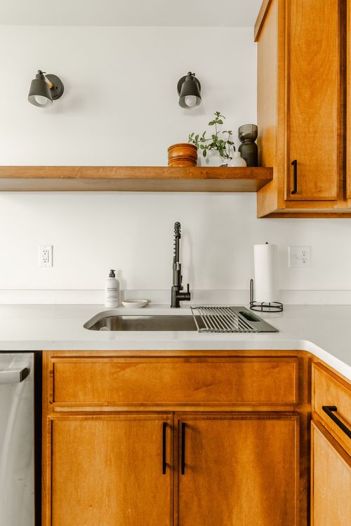 Close view of a kitchen sink with black faucet, quartz counter and open wood shelf