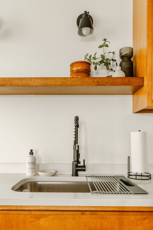 Detail of a black gooseneck kitchen faucet with a wood shelf and potted plant above