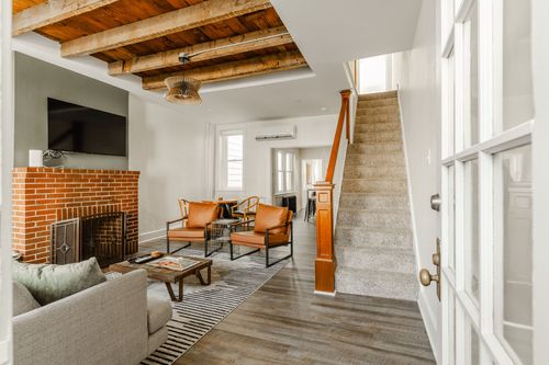 Living room with a brick fireplace, mounted TV, wood beam ceiling and tan leather chairs