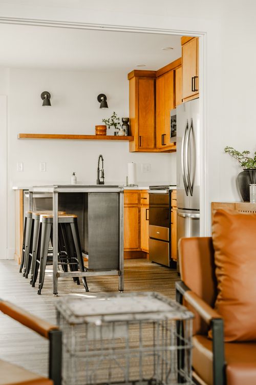 Kitchen with a metal island, barstools and a living room with leather chairs visible beyond