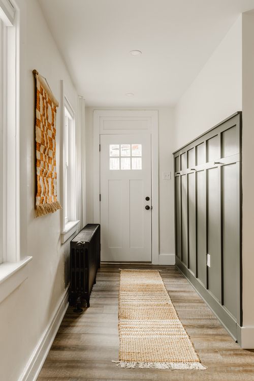 Entry hallway with a woven wall hanging, black radiator and dark paneled wainscoting
