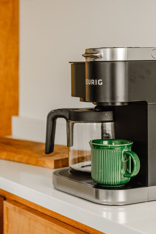 Close view of a black Keurig coffee maker with a green ceramic mug