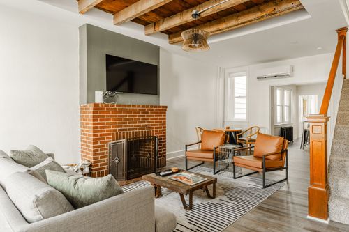 Living room with brick fireplace, leather accent chairs, striped rug and an open staircase