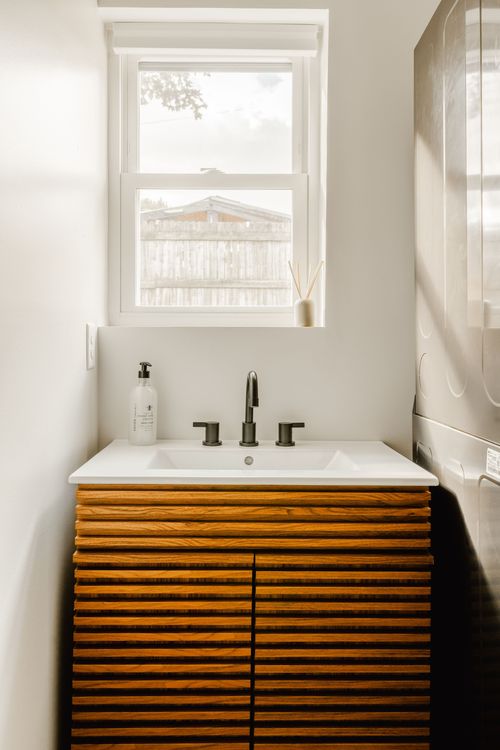 Fluted wood vanity with a white sink top, matte-black faucet and window above
