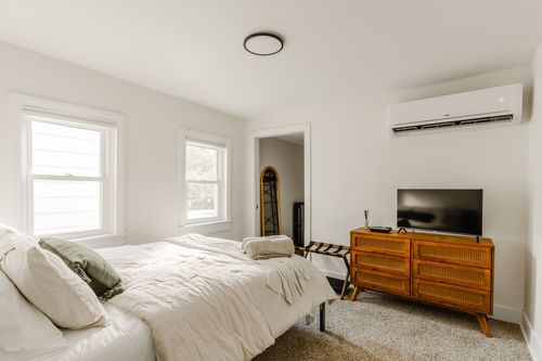 Bright bedroom with white linens, a mid-century dresser and wall-mounted TV