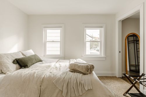 Bedroom with a sage green pillow, neutral linens and two tall windows