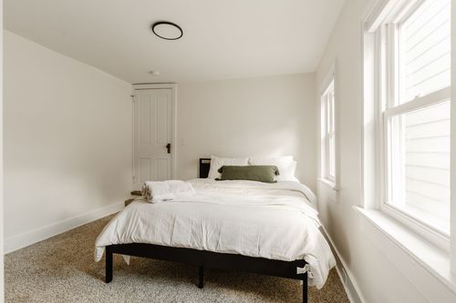 Bedroom with a black platform bed, white paneled door and neutral carpet
