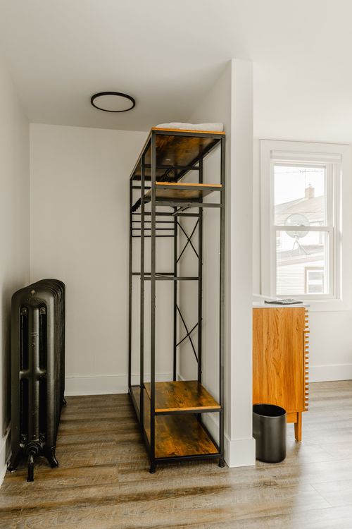 Open industrial-style wardrobe rack beside a black radiator and wood dresser