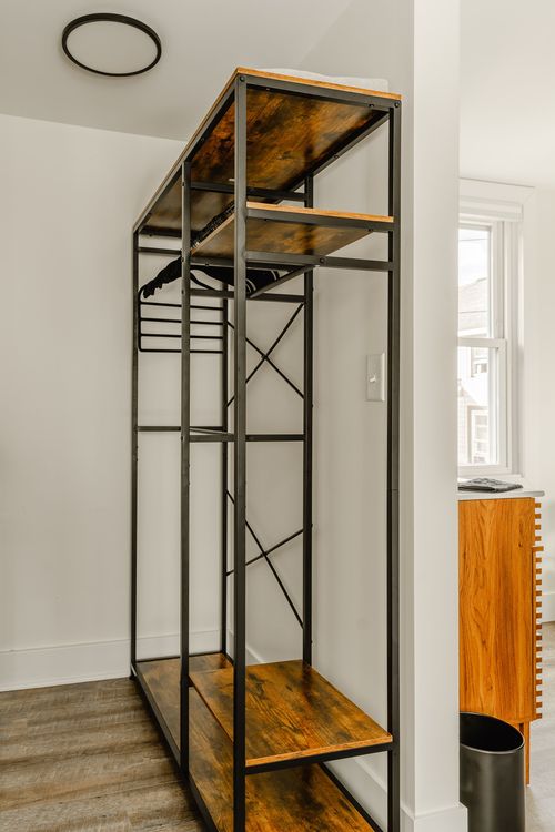 Open black metal wardrobe rack with wood shelves and hanging clothes